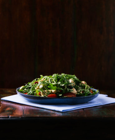 Fresh salad with arugula, cherry tomatoes and feta cheese in blue plate over dark wooden backgroundの写真素材