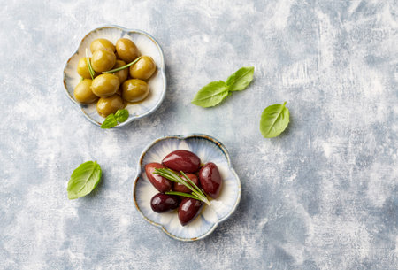 Pickled green olives with basil leaves on a stone background. Selective focus.