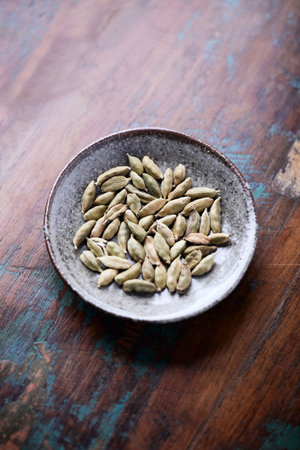 Dried cardamom seeds in a bowl on rustic wooden background