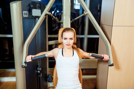 sport, fitness, lifestyle and people concept - young woman flexing muscles on gym machine.の写真素材
