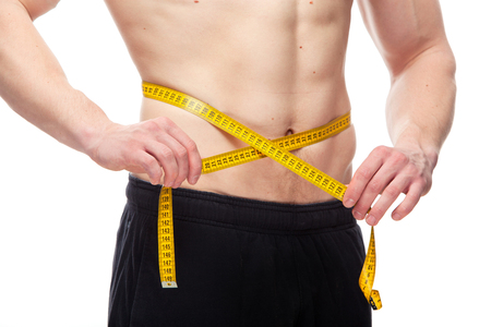 Fit man measuring his waist after a workout in the gym, isolated in a white background.の写真素材