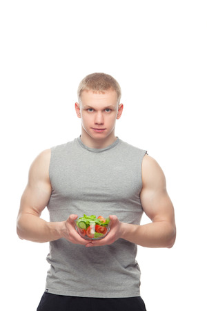 Young happy muscular man eating a salad over white backgroundの写真素材