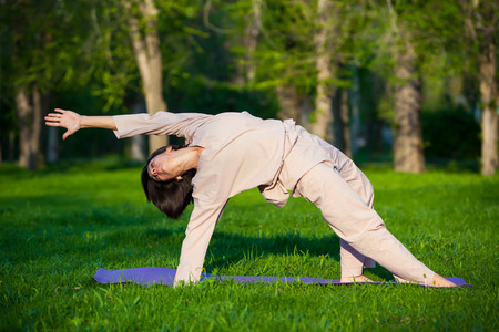 Yoga utthita trikonasana triangle pose by woman in white costume on green grass in the park around pine treesの写真素材