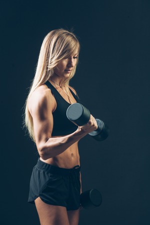 Athletic woman with dumbbells on a dark backgroundの写真素材