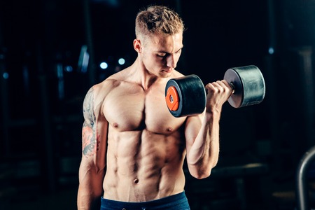 Athlete muscular bodybuilder training back with dumbbell  in the gym.
