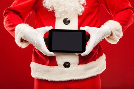 Santa Claus holding tablet on red backgroundの写真素材