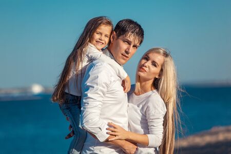 Young family in blue jeans hugging on the background of water.の写真素材