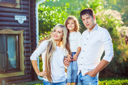 Happy family with child outdoors, against the background of a wooden house. in jeansの写真素材