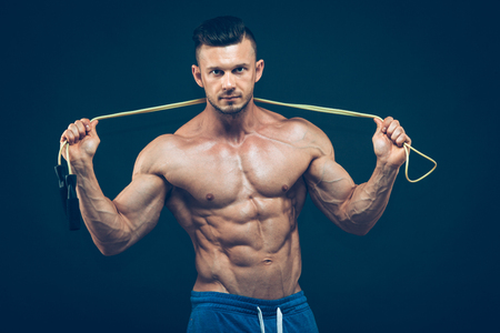 Muscular man skipping rope. Portrait of muscular young man exercising with jumping rope on black background.の写真素材