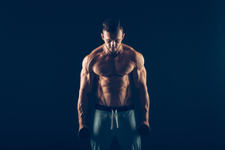 Closeup of a muscular young man lifting dumbbells weights on dark background .の写真素材