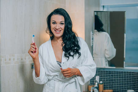 Portrait of attractive woman brushing teeth in bathroom in a white coat. healthy teeth.