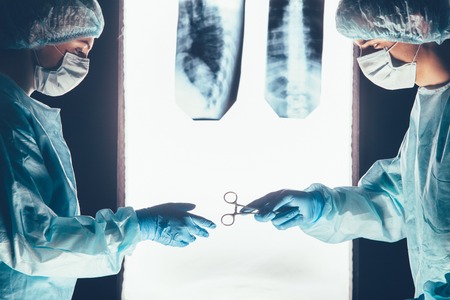 Two surgeons working and passing surgical equipment in the operating room hospital healthcare  against the background of the spine X-raysの写真素材