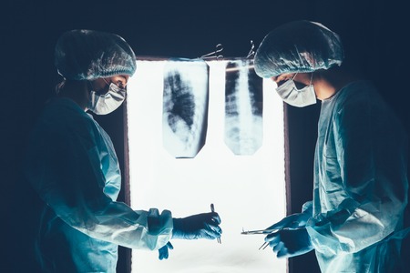 Two surgeons working and concentrating at operating table. Medical team in hospital performing operation. Group of surgeon at work in operating theatre room. healthcar. against the background of the spine X-raysの写真素材