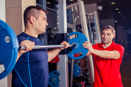 sport, fitness, teamwork, bodybuilding and people concept - man and personal trainer with barbell flexing muscles in gymの写真素材