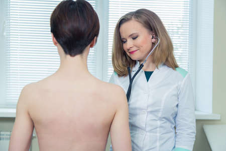 Doctor listening to patients chest with stethoscope in his office at the hospital.の写真素材