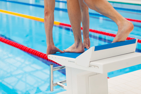 Young muscular swimmer in low position on starting block in a swimming pool.の写真素材