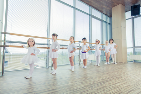 Group of seven little ballerinas standing in row and practicing ballet and using stick on the wall. They are good friend and amazing dance performersの写真素材