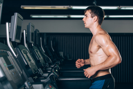 Young man in sportswear running on treadmill at gym.