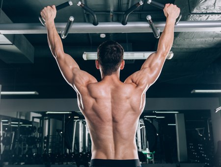 Athlete muscular fitness male model pulling up on horizontal bar in a gym.