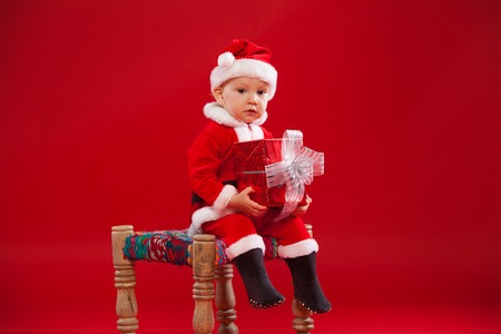 Beautiful little baby celebrates Christmas. New Year's holidays. Baby in a Christmas costume with giftの写真素材