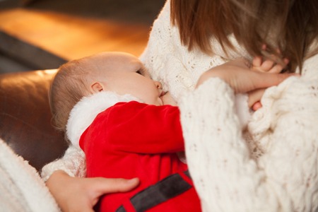 Newborn baby wearing as Santa Claus breast feeding. Selective focus on the kid s face. Homemade...