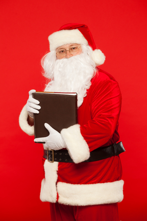 Santa Claus reads old book, on a red background. Christmas.の写真素材