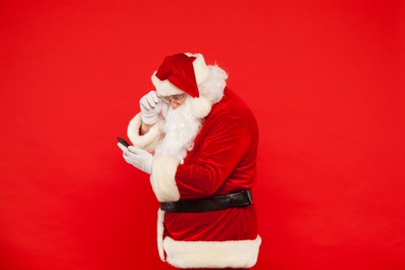 Photo of Santa Claus using mobile phone, on a red background. Christmas.の写真素材