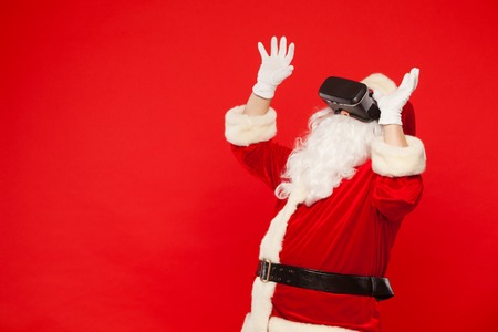 Santa Claus wearing virtual reality goggles, on a red background. Christmas.の写真素材
