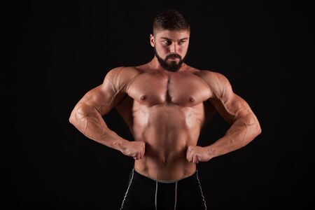 Rear view of healthy muscular young man with his arms stretched out isolated on black background.