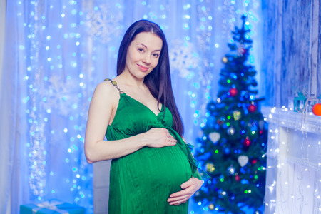 Pregnant woman happy at home near the Christmas tree during the Christmas celebrationの写真素材