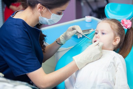 Close-up of pretty little girl opening his mouth wide during inspection of oral cavity at the dentistの写真素材