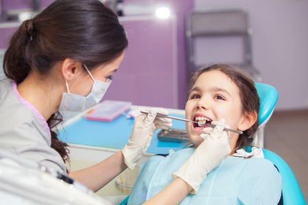 Close-up of pretty little girl opening his mouth wide during treating her teeth by the dentistの写真素材