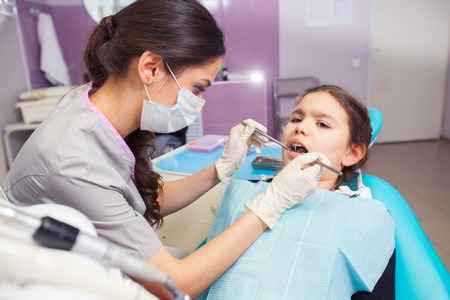 Close-up of pretty little girl opening his mouth wide during treating her teeth by the dentistの写真素材