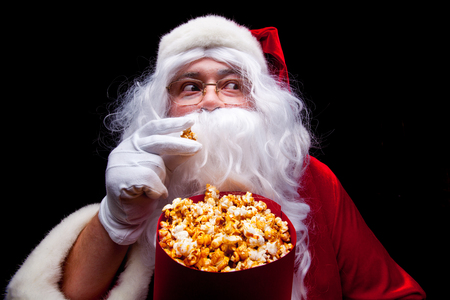Christmas. Photo of Santa Claus gloved hand With a red bucket with popcorn, on a black backgroundの写真素材