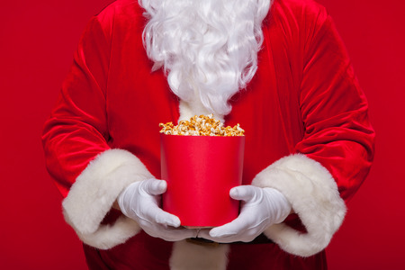 Christmas. Photo of Santa Claus gloved hand With a red bucket with popcorn, on a red backgroundの写真素材