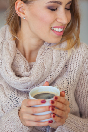 Beautiful woman holding a cup of coffee in her hands. in a knitted beige sweaterの写真素材
