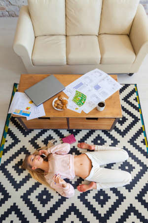 Pretty young blonde studying on her laptop while lying in her living room. He lies on his back, a...
