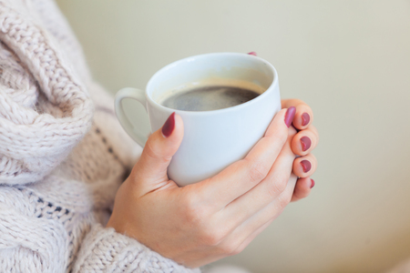Beautiful woman holding a cup of coffee in her hands. in a knitted beige sweaterの写真素材