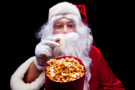 Christmas. Photo of Santa Claus gloved hand With a red bucket with popcorn, on a black backgroundの写真素材
