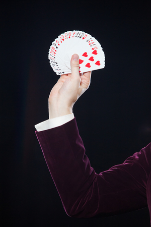 Hand with cards close-up. Midsection of magician showing fanned out cards against black background....