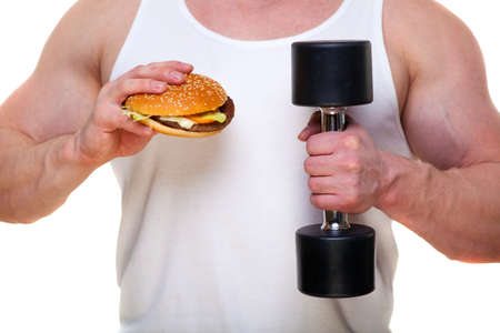 Fat man with a hamburger holds dumbbells isolated on white. The concept of choosing between harmful food and a healthy lifestyle. Portrait of overweight person who spoiled healthy meal . Junk meal leads to obesity. Disruption from diet concept. He is trying to go on a diet.の写真素材