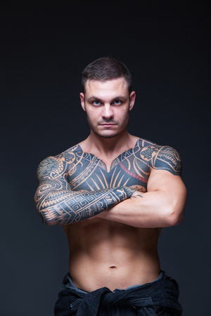 The man with a muscular naked torso with tattoos on the dark background. ABSの写真素材