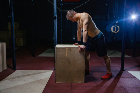 Portrait of fatigued fitness guy. Near the wooden cube. Cross fit style.の写真素材