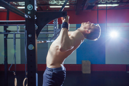 Athlete muscular fitness male model pulling up on horizontal bar in a gym. Cross fit style