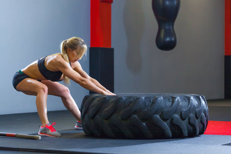 Fit female athlete working out with a huge tire, pulls in the gym. Crossfit woman exercising with big tireの写真素材