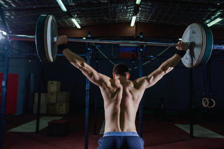 Portrait of a handsome athlete from behind. Athlete raises the barbell over your head. Studio shots in the dark tone. Cross style fit, deadliftの写真素材