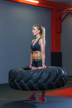 Fit female athlete working out with a huge tire, turning and carry in the gym. Crossfit woman exercising with big tireの写真素材