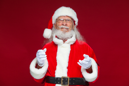 Christmas. Good Santa Claus in white gloves shows faces, grimaces, shows his tongue. Not standard behavior. Isolated on red background.の写真素材