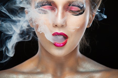 Halloween. Portrait of young beautiful girl with make-up. E-cigarette smoke, Viper. Isolated on black background.の写真素材