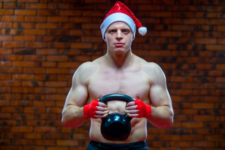 Christmas. Muscular Fighter kickbox boxing Santa Claus With Red Bandages the background of a brick wall. Holds sports equipment in his handsの写真素材